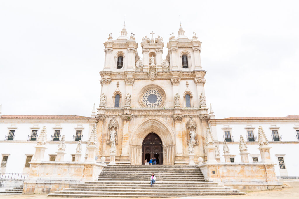 Shivani sits in front of the Monastery of Santa Maria in Alcobaça, marveling at its stunning architecture and historical significance